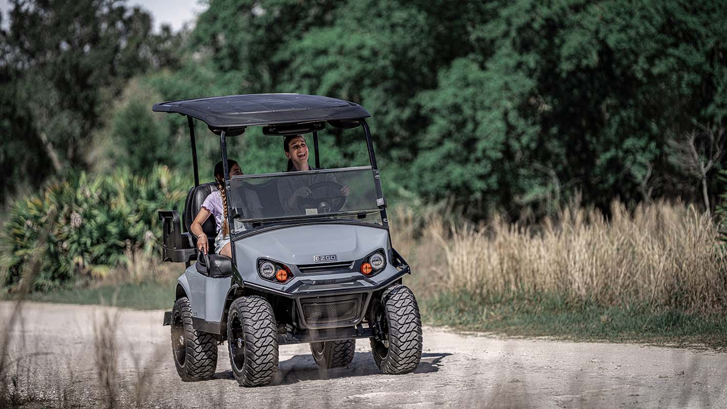 An E-Z-GO golf cart being driven down a paved path.